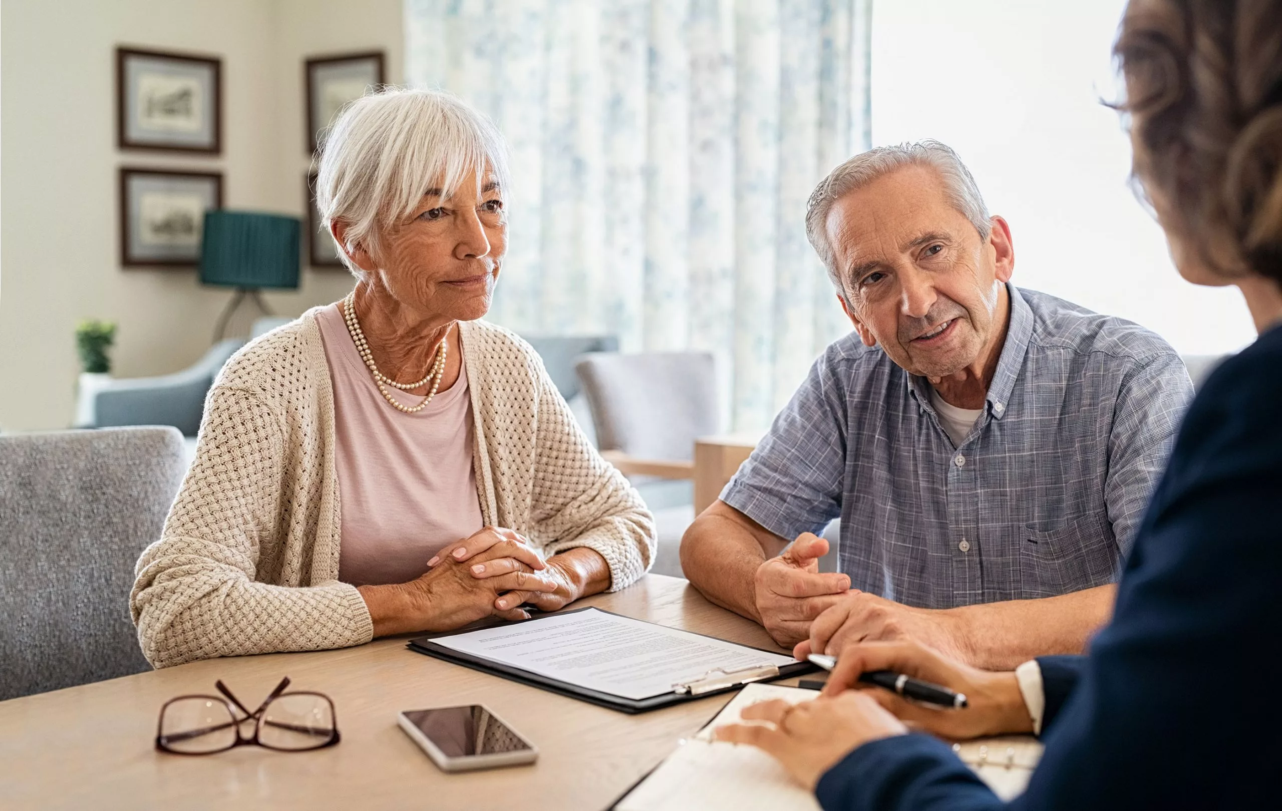 Zwei ältere Personen um die 70 Jahre werden von einer Pflegekraft beraten und schauen diese an.