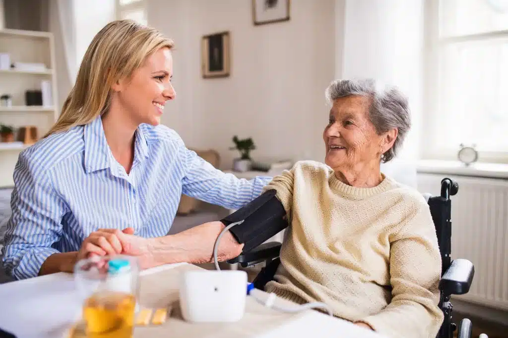 Ältere Dame wird von einer Pflegekraft untersucht und freundlich betreut. Es findet ein Gespräch statt. Beide lächeln sich an.