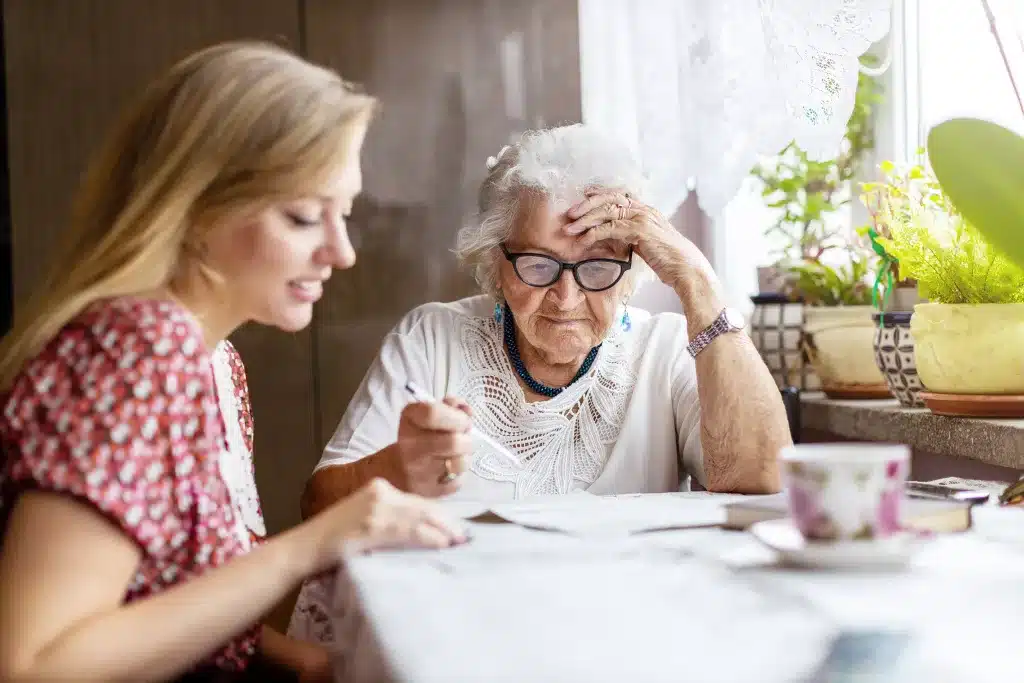 Eine Pflegekraft unterstützt eine ältere Frau bei schriftlichen Unterlagen. Die Seniorin ist sehr konzentriert..