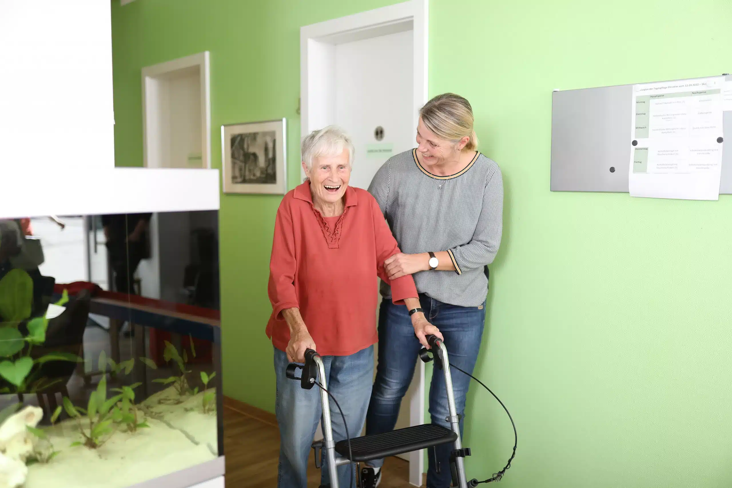 Eine Pflegekraft unterstützt eine Seniorin die einen Rolator zum gehen nutzt. 