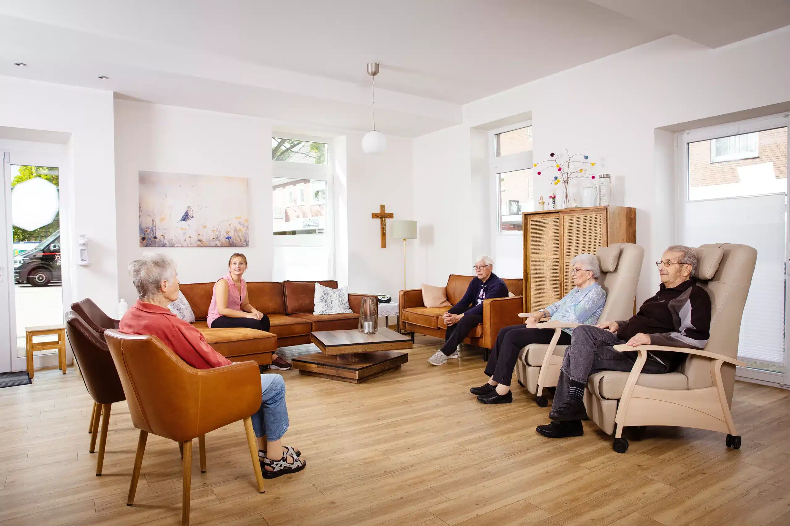 Gemeinschaftsraum in der Tagespflege von Leusbrock Pflege. Menschen sitzen gemütlich und unterhalten sich.
